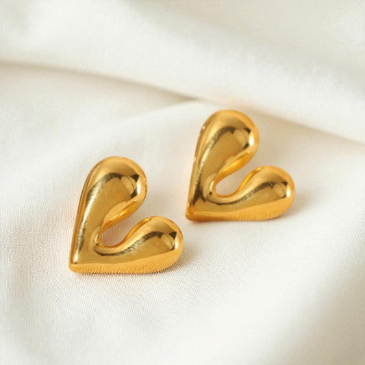 Gold heart-shaped earrings on a white fabric background Orlaya Jewellery