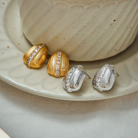 Vintage-inspired gold stud earrings with ridged texture and central crystal accents, styled on a ceramic plate with a neutral backdrop