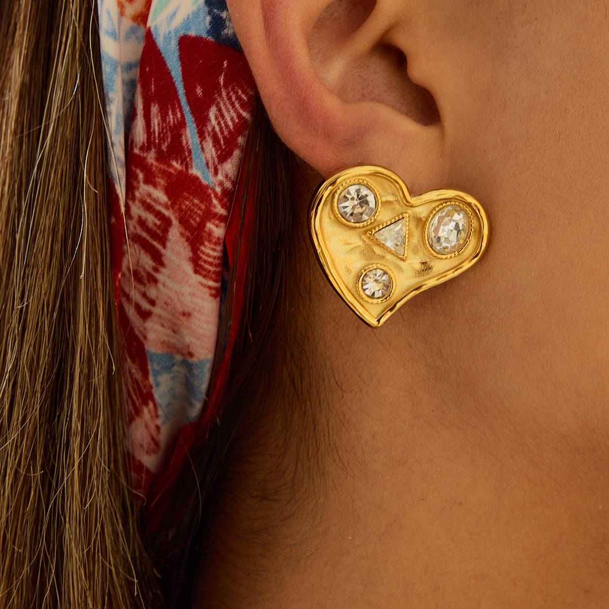 Gold heart-shaped earring with gemstones worn by a person Orlaya Jewellery