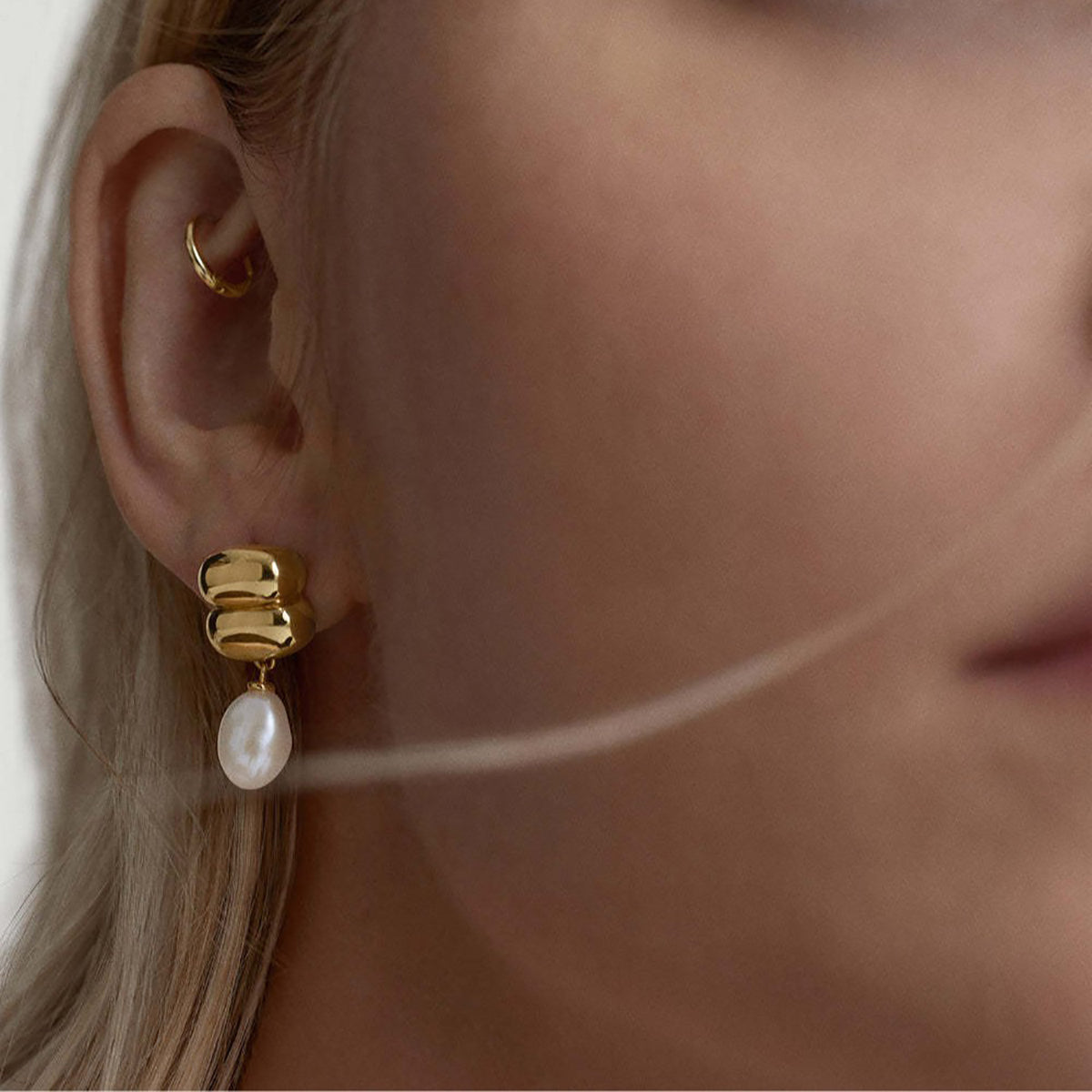 Close-up of a model wearing pearl drop earrings with sculpted gold detailing