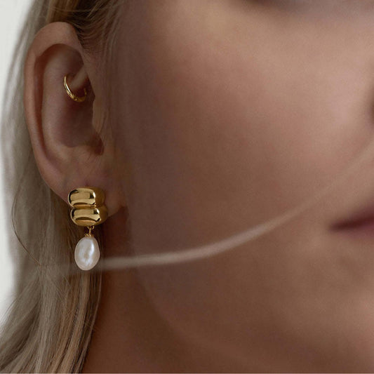 Close-up of a model wearing pearl drop earrings with sculpted gold detailing