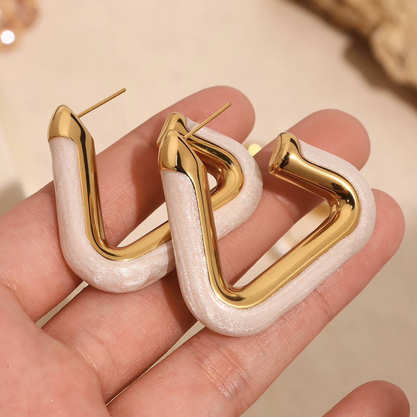 Gold and white hoop earrings held in a hand against a neutral background Orlaya Jewellery
