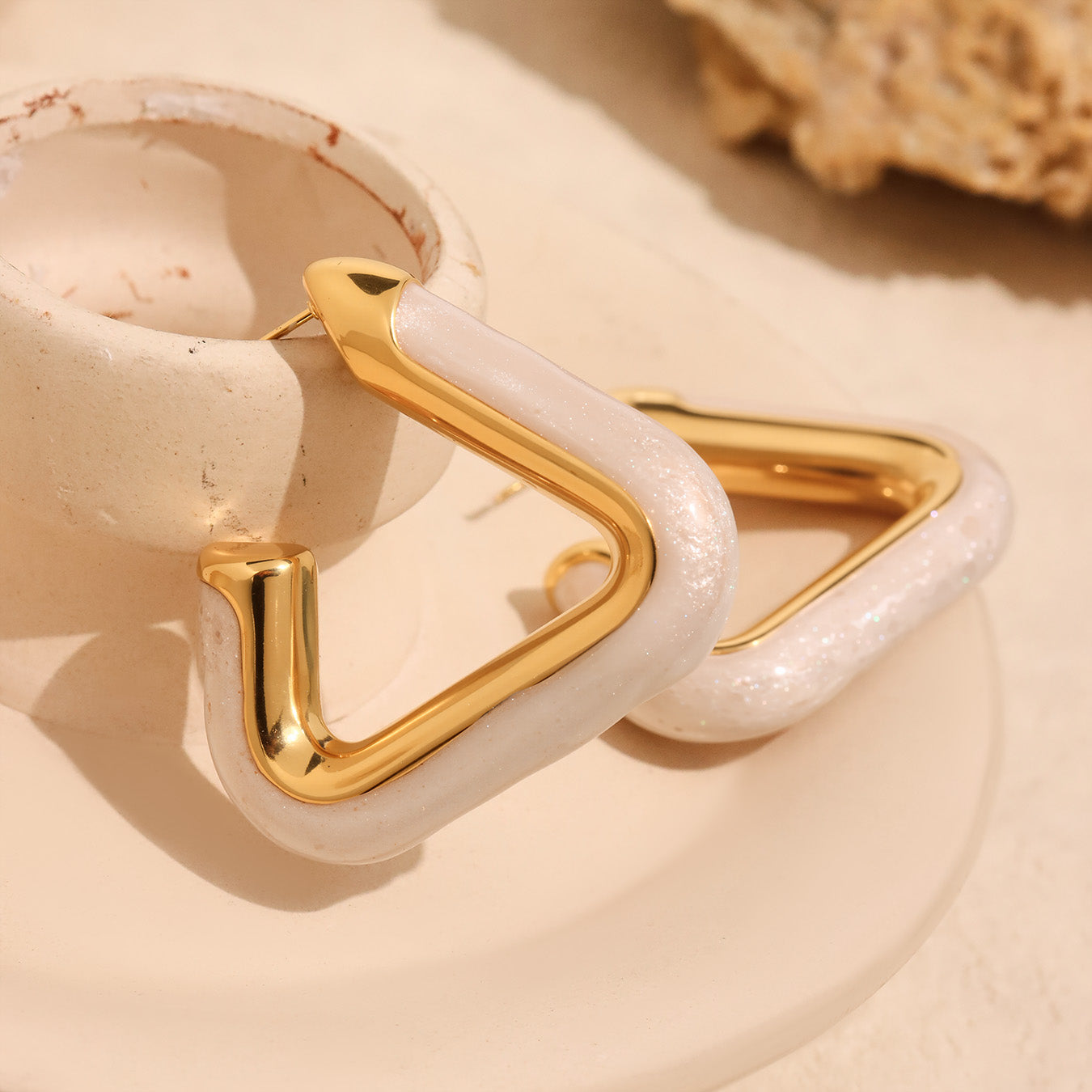 Close-up of Nova Edge 18K gold-plated geometric hoop earring with pearly white detail on beige background – Orlaya Jewellery.