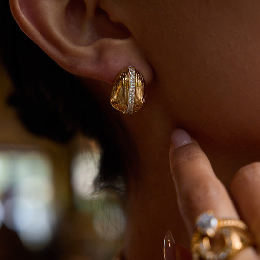 Vintage-inspired gold stud earring with ridged texture and central crystal accent, worn by a model