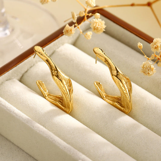 Zephyr gold sculptural hoop earrings on textured beige surface